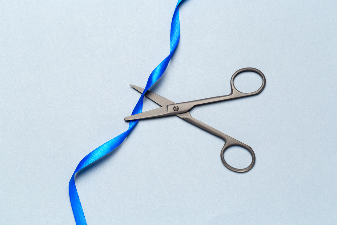 Grand Opening illustrated with scissors and a blue ribbon on a gray background
